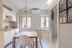 A modern kitchen with white cabinets, a dining table with chairs, and large windows. - A Romantic Roman Getaway: Elegant Apartment Steps from the Vatican (Roma)