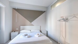 A modern hotel room with a large bed, white bedding, a bedside table, and a hanging clothes rack. - A Romantic Roman Getaway: Elegant Apartment Steps from the Vatican (Roma)