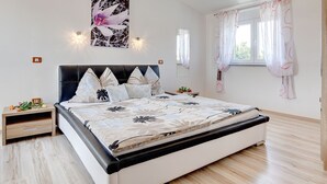 A bedroom with a bed, a nightstand, a wall-mounted light fixture, a window with curtains, and a wall-mounted mirror. - Villa Marcelia by Interhome (Bokordici)