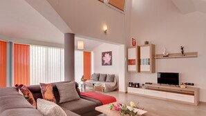 A modern living room with a sectional sofa, a coffee table with flowers, a TV, and built-in shelving. - Villa Marcelia by Interhome (Bokordici)
