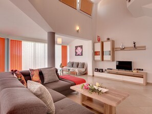 Ein modernes Wohnzimmer mit einer Eckcouch, einem Couchtisch mit Blumen, einem Fernseher und Einbauschränken.