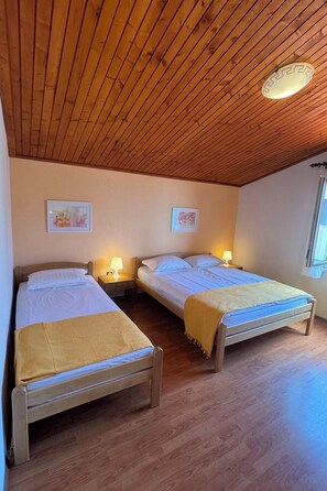 Ein Zimmer mit zwei Holzbettgestellen, jeweils mit Nachttisch und Lampe, und einer Decke mit Holzbalken.