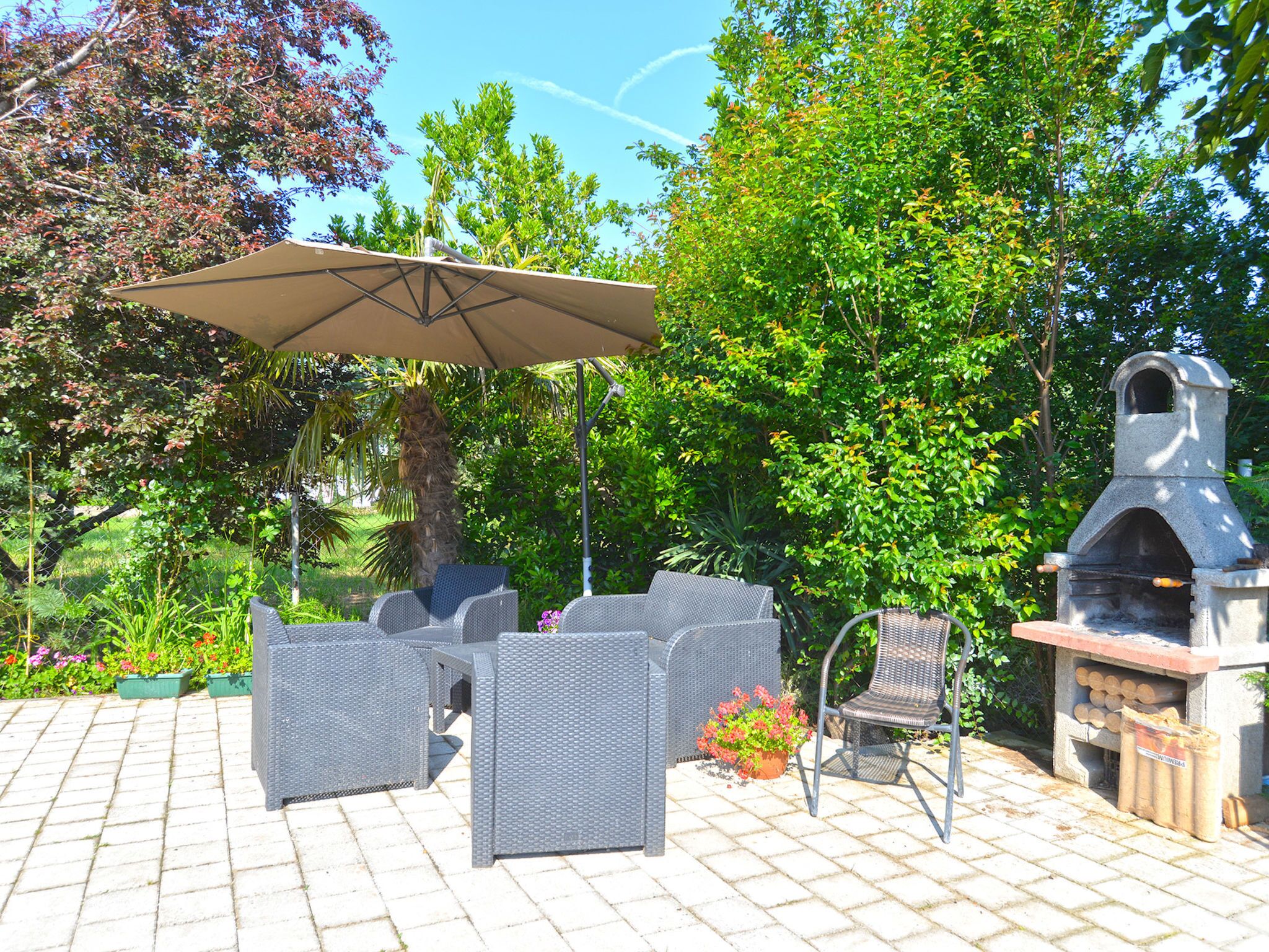 Een terras buiten met rieten meubilair, een grote parasol en een stenen barbecue.