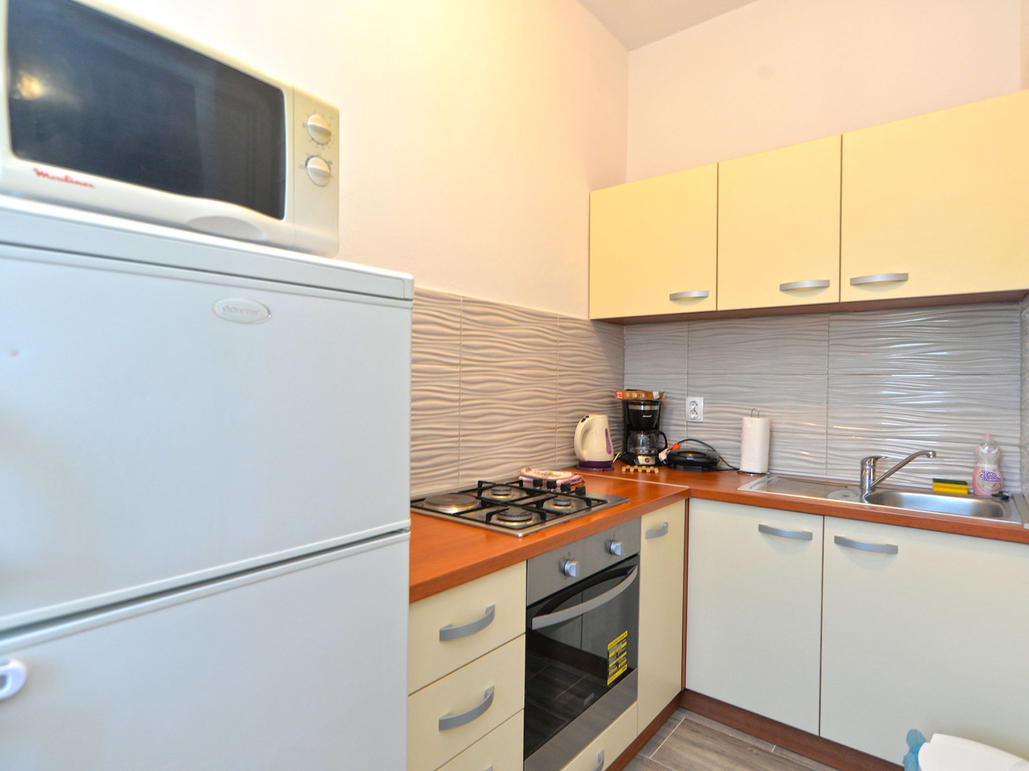 A compact kitchen with a microwave, stove, oven, and a kettle on the countertop.