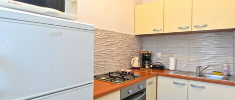 A compact kitchen with a microwave, stove, oven, and a kettle on the countertop.