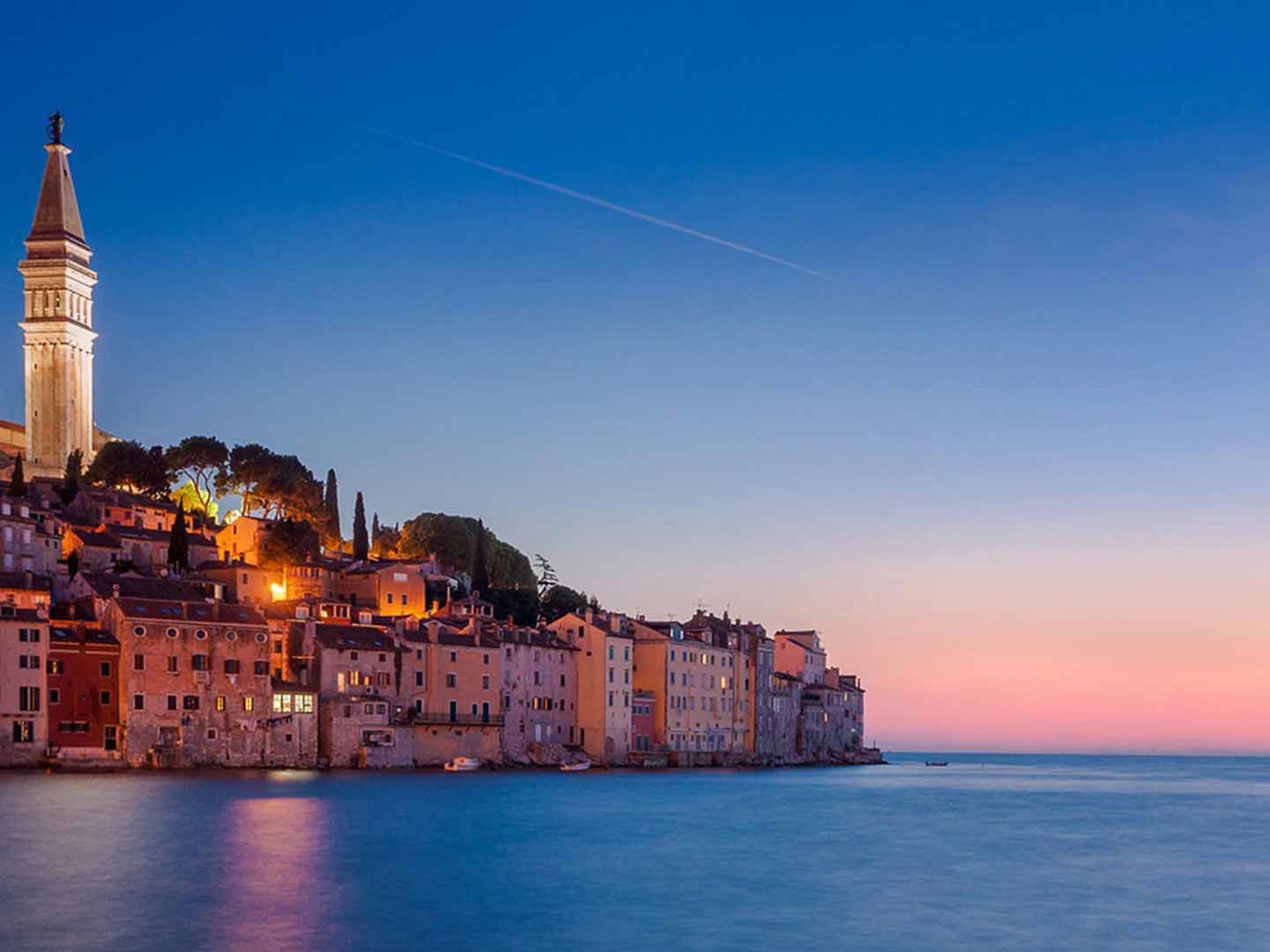 A coastal town with historic buildings, a prominent tower, and calm waters.