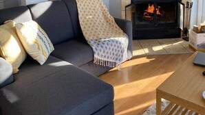 A living room with a dark grey sofa, a patterned throw blanket, and a fireplace with a visible fire. - Bleuzen • Vue splendide • 2 chambres • Foyer • Balcon (Petite-Rivière-Saint-François)