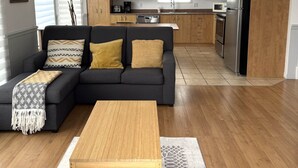 A modern living room with a sectional sofa, wooden coffee table, and a kitchen with wooden cabinets and stainless steel appliances. - Bleuzen • Vue splendide • 2 chambres • Foyer • Balcon (Petite-Rivière-Saint-François)