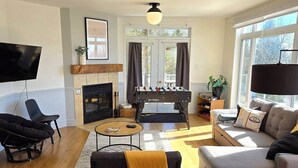 A living room with a fireplace, sofa, armchair, coffee table, and a foosball table. - Bleuzen Charlevoix • 3 chambres • 2 salle-de-bain • SPA privé • Foyer • Terrasse (Petite-Rivière-Saint-François)
