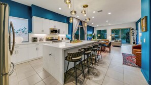 A modern kitchen with white cabinets, a central island with bar stools, and pendant lighting. - Golf n Grooves. Luxury La Quinta Villa. (La Quinta)
