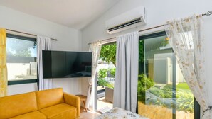 A modern room with a sofa, a flat-screen TV, and a bed with a floral bedspread. - Mango Gardens - Tropical Living Made Simple (Oranjestad)