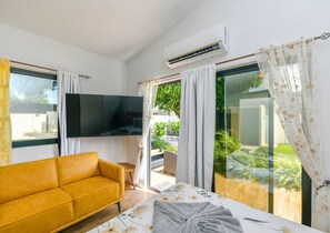 A modern room with a sofa, a flat-screen TV, and a bed with a floral bedspread. - Mango Gardens - Tropical Living Made Simple (Oranjestad)