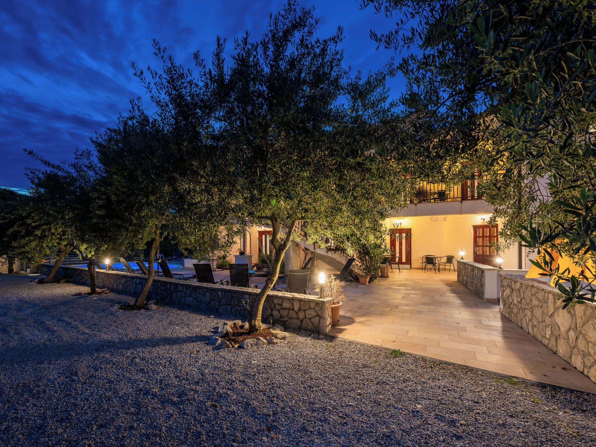 Une villa avec un chemin de pierre menant à un patio couvert, entouré d’arbres et d’une piscine.