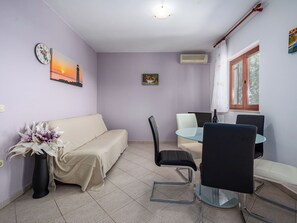 Ein Zimmer mit einer Couch, Sesseln, einem Tisch, einer Uhr und einem Fenster.