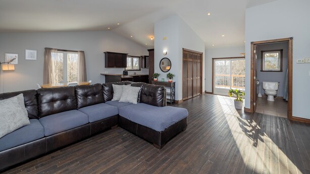 A spacious living area with a sectional sofa, a kitchen in the background, and a view of the outside. - The Bognor House (Meaford)