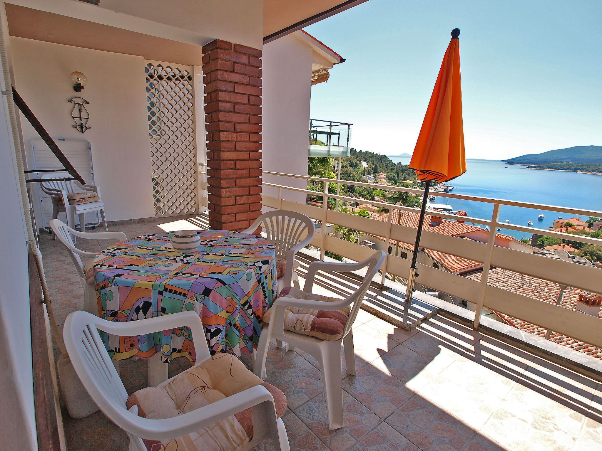 Un balcón con mesa, sillas y una sombrilla con vista al mar.