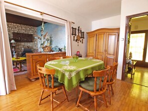 A dining room with a green tablecloth, wooden chairs, a fireplace, and a view of the outside. - Apartment 155 by Interhome (Rabac)