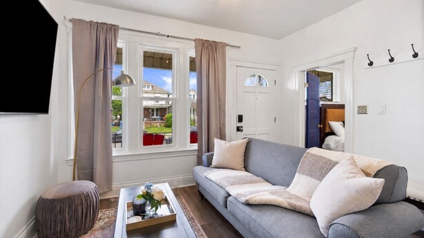 Ein Wohnzimmer mit grauem Sofa, einem Couchtisch mit Tablett, einem runden Ottomanen und Blick ins Freie.