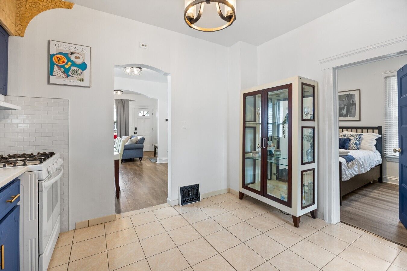 Une cuisine moderne équipée d’une cuisinière à gaz, un coin repas avec un canapé bleu et une chambre à coucher avec un lit et des stores aux fenêtres.