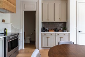 A modern kitchen with white cabinetry, a wooden dining table, and a built-in stove.
