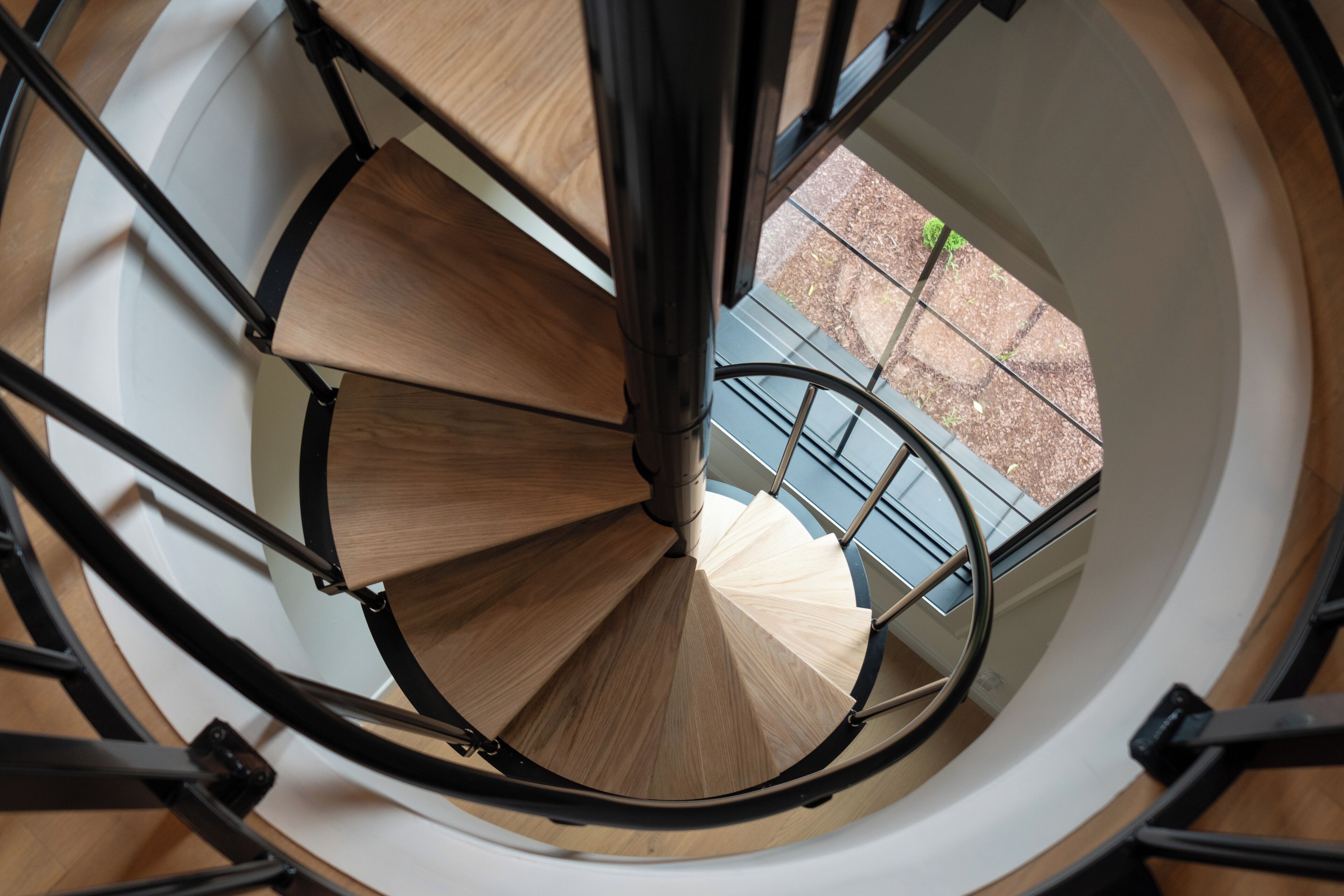 Un escalier en colimaçon avec des marches en bois et des rampes en métal, menant à un espace extérieur doté d’une rambarde bleue.