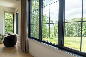 A room with large windows, a dark chair, and a small table with books. - NEW - Private Hilltop Retreat • Hot Tub • Stunning Views • King Suite (Columbia)