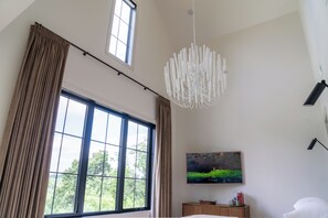 A bedroom with a large window, a painting on the wall, and a modern chandelier. - NEW - Private Hilltop Retreat • Hot Tub • Stunning Views • King Suite (Columbia)