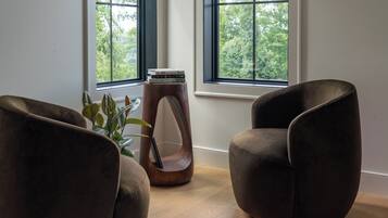 Une pièce avec deux fauteuils marron, une table d’appoint en bois sur laquelle sont posés des livres, et une plante en pot.