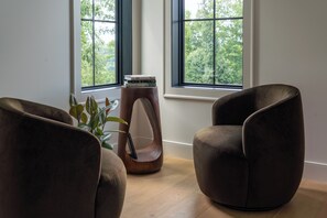 A room with two brown armchairs, a wooden side table with books, and a potted plant.