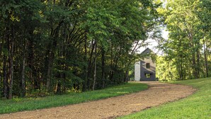 Ein Kiesweg führt zu einem Steinhaus, das von dichten Bäumen umgeben ist.