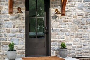 A stone facade with a dark-colored door, two potted plants, and wall-mounted lighting fixtures. - NEW - Private Hilltop Retreat • Hot Tub • Stunning Views • King Suite (Columbia)