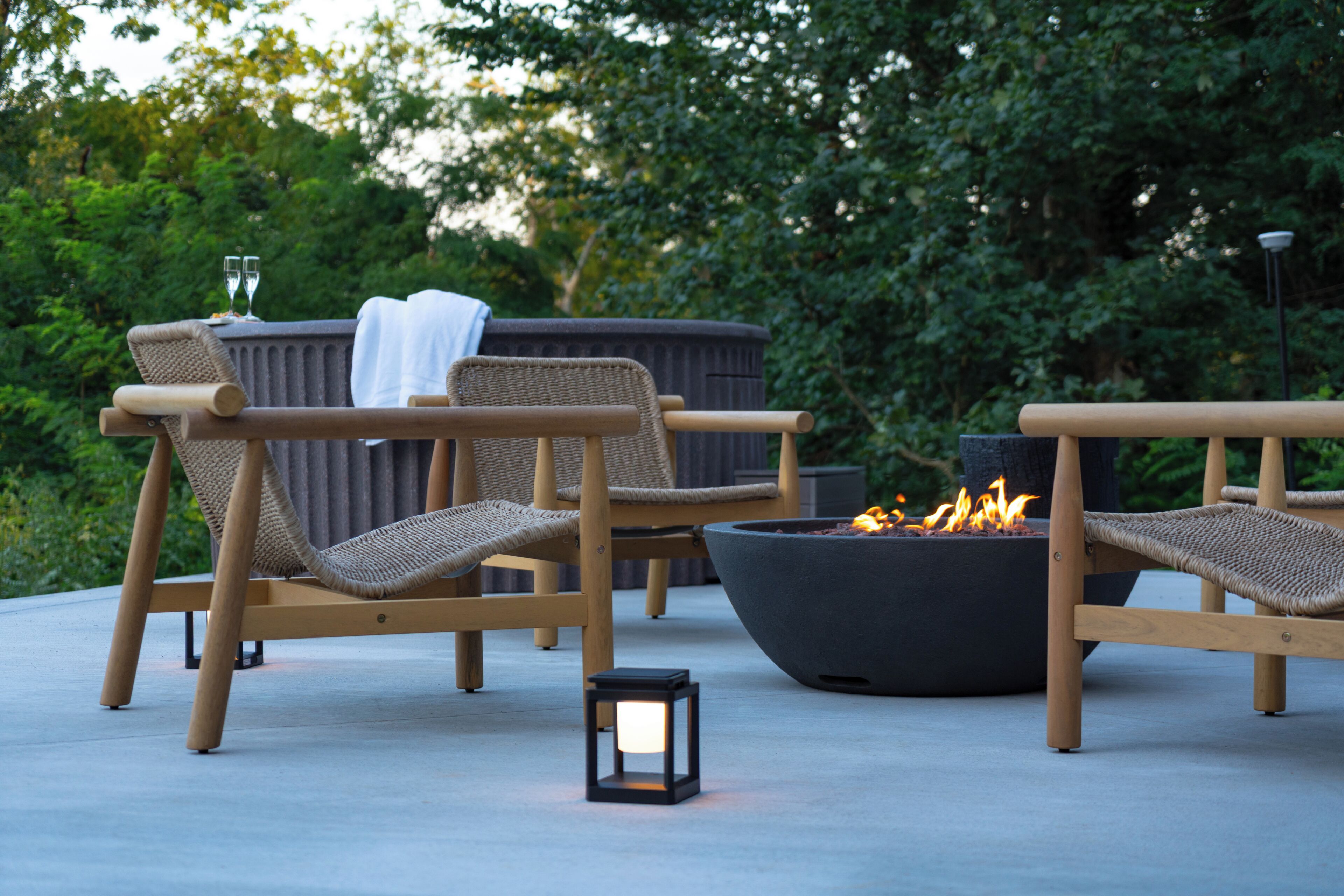 Deux fauteuils de jardin en osier avec des coussins, un foyer noir et une petite table avec des verres.