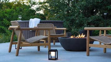 Deux fauteuils de jardin en osier avec des coussins, un foyer noir et une petite table avec des verres.