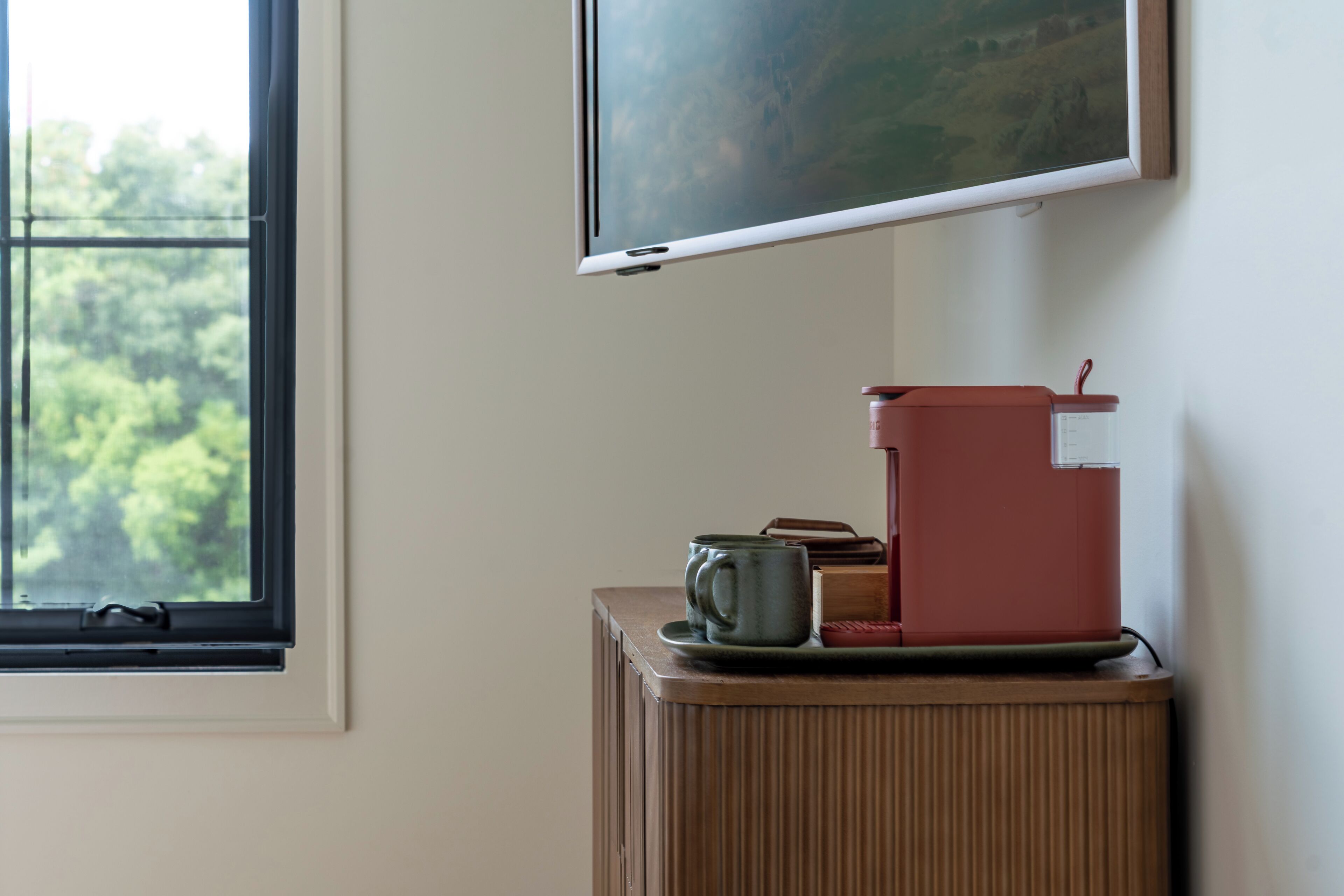 Ein Zimmer mit Fenster, Wandfernseher und einer Kaffeemaschine auf einem Schrank.