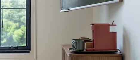 A room with a window, a wall-mounted television, and a coffee machine on a cabinet.
