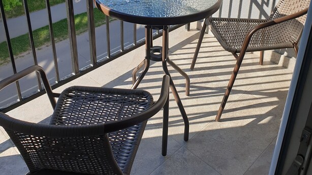 Een klein balkon met een ronde glazen tafel en twee rieten stoelen.
