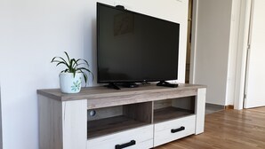 Een houten tv-meubel met een flatscreen televisie, een bloempot en twee lades.