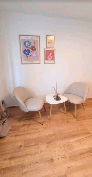 A room with two beige armchairs, a small round table with a candle, and framed artwork on the wall. - Merci vacation apartment (Niestetal)