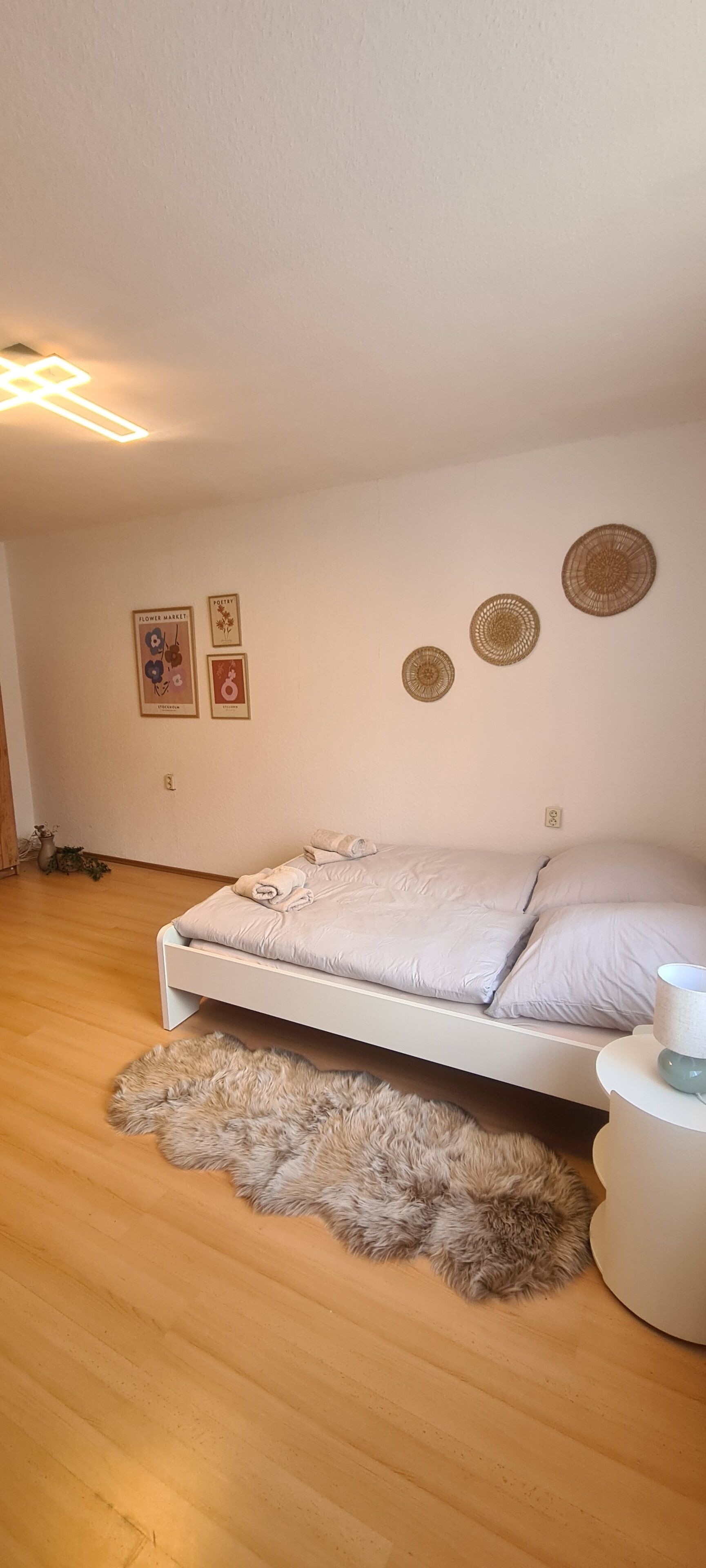 Een slaapkamer met een bed, een zacht tapijt, wanddecoratie en een nachtkastje met een lamp.