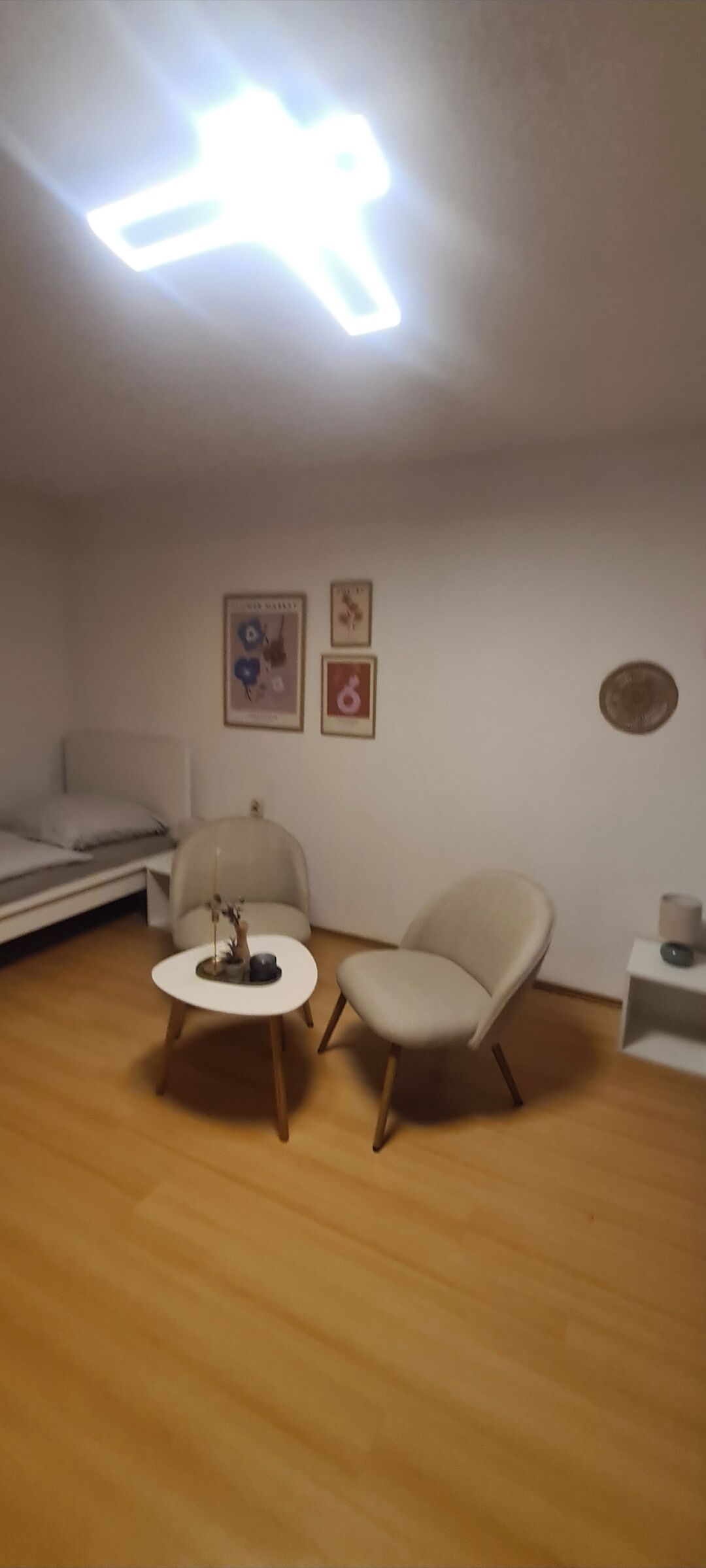A small, modern room with a round table and two chairs, a sofa, and a ceiling light fixture.