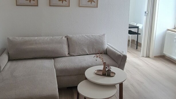 A modern living room with a sectional sofa, a round coffee table, and three framed artworks on the wall. - Merci vacation apartment (Niestetal)