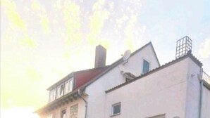 A two-story building with a flat roof, a satellite dish, and a gated entrance. - Merci vacation apartment (Niestetal)