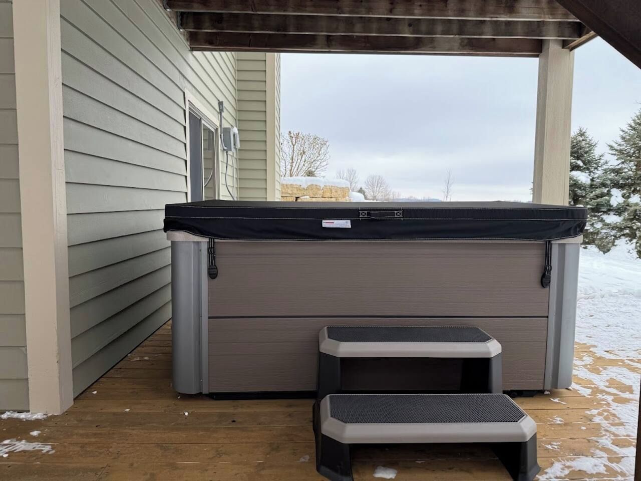 A hot tub with a cover, a small table, and a step stool in front of a house.