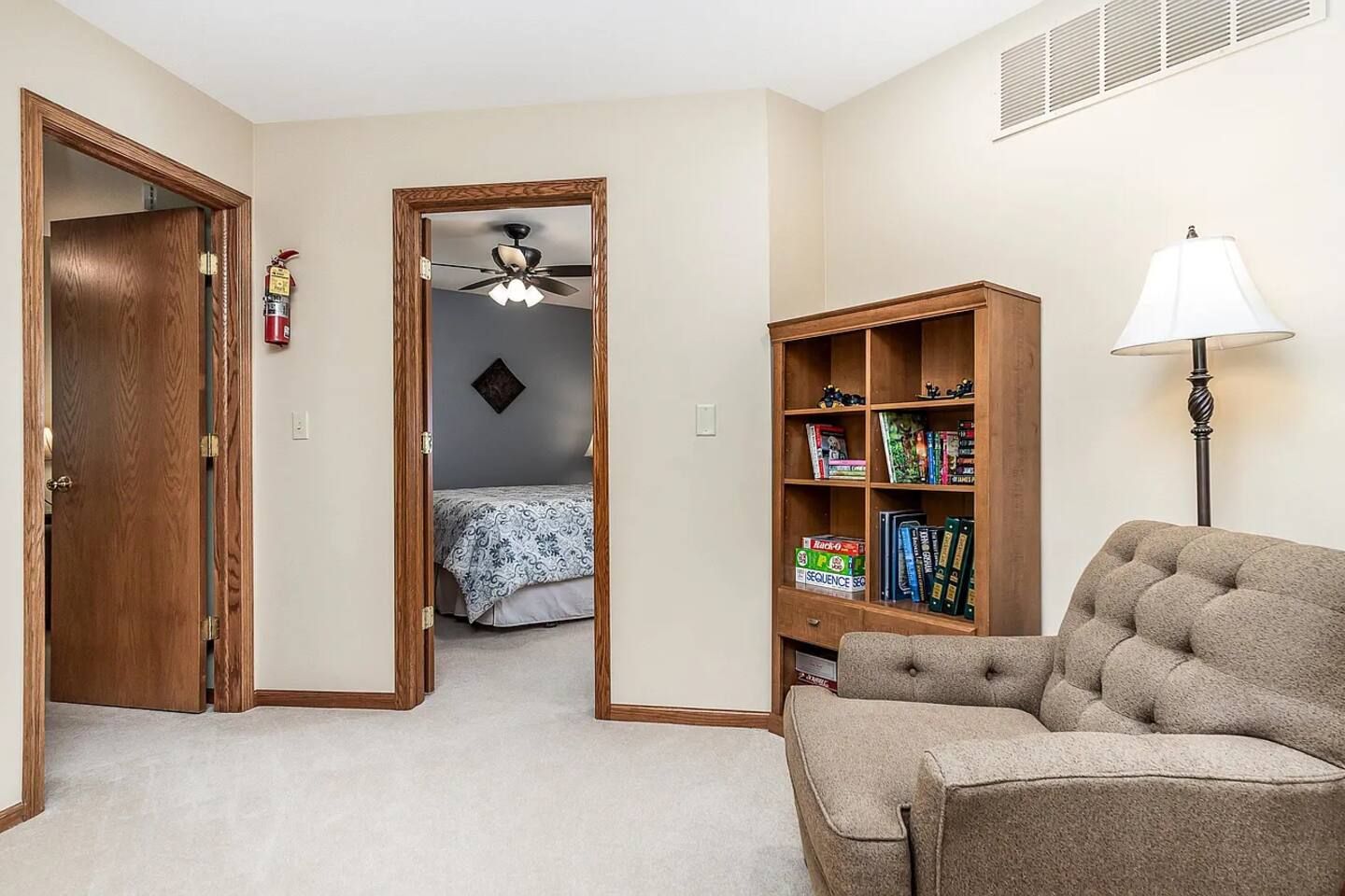 Ein Zimmer mit Holztür, Bücherregal, Lampe und Stuhl.