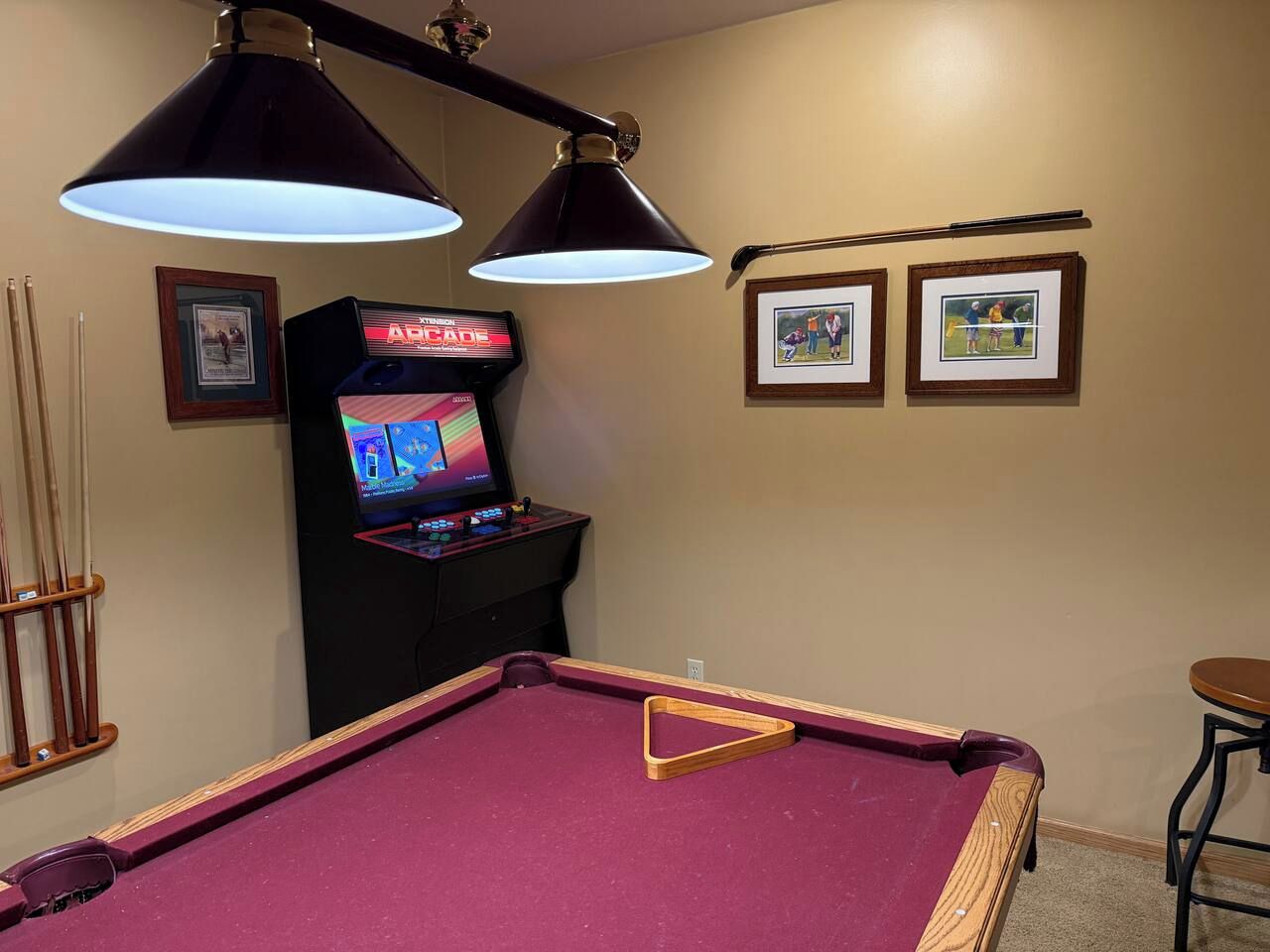 A pool table with overhead lighting, a pool cue rack, and a video game machine.