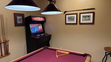 A pool table with overhead lighting, a pool cue rack, and a video game machine.