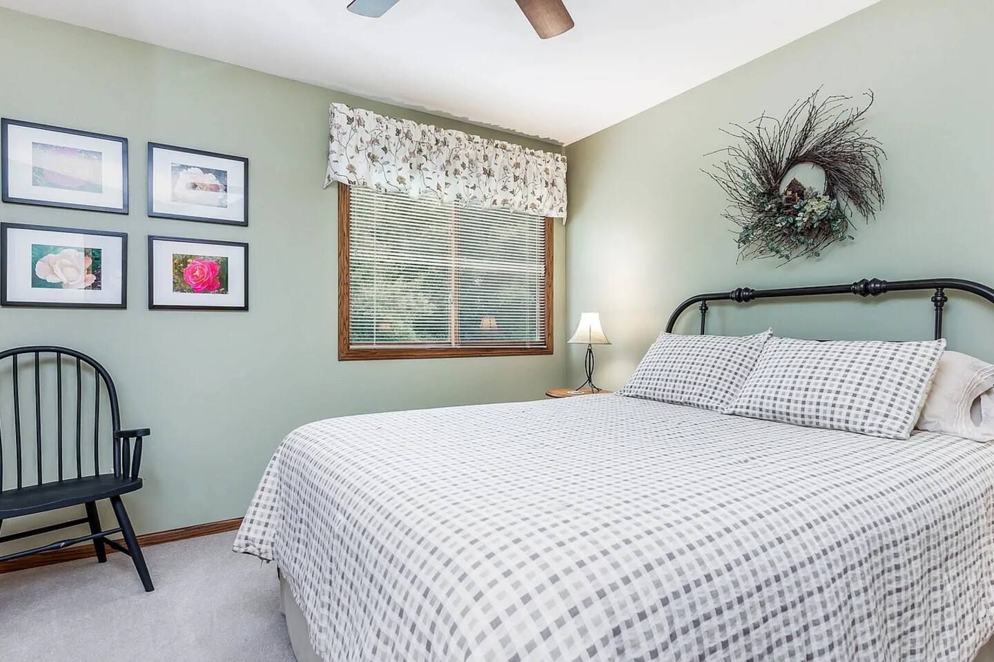 A bedroom with a bed, a chair, a window with blinds, and wall decorations.