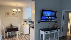 Uma cozinha moderna com forno embutido, mesa de jantar com cadeiras e TV na parede exibindo diversos canais.