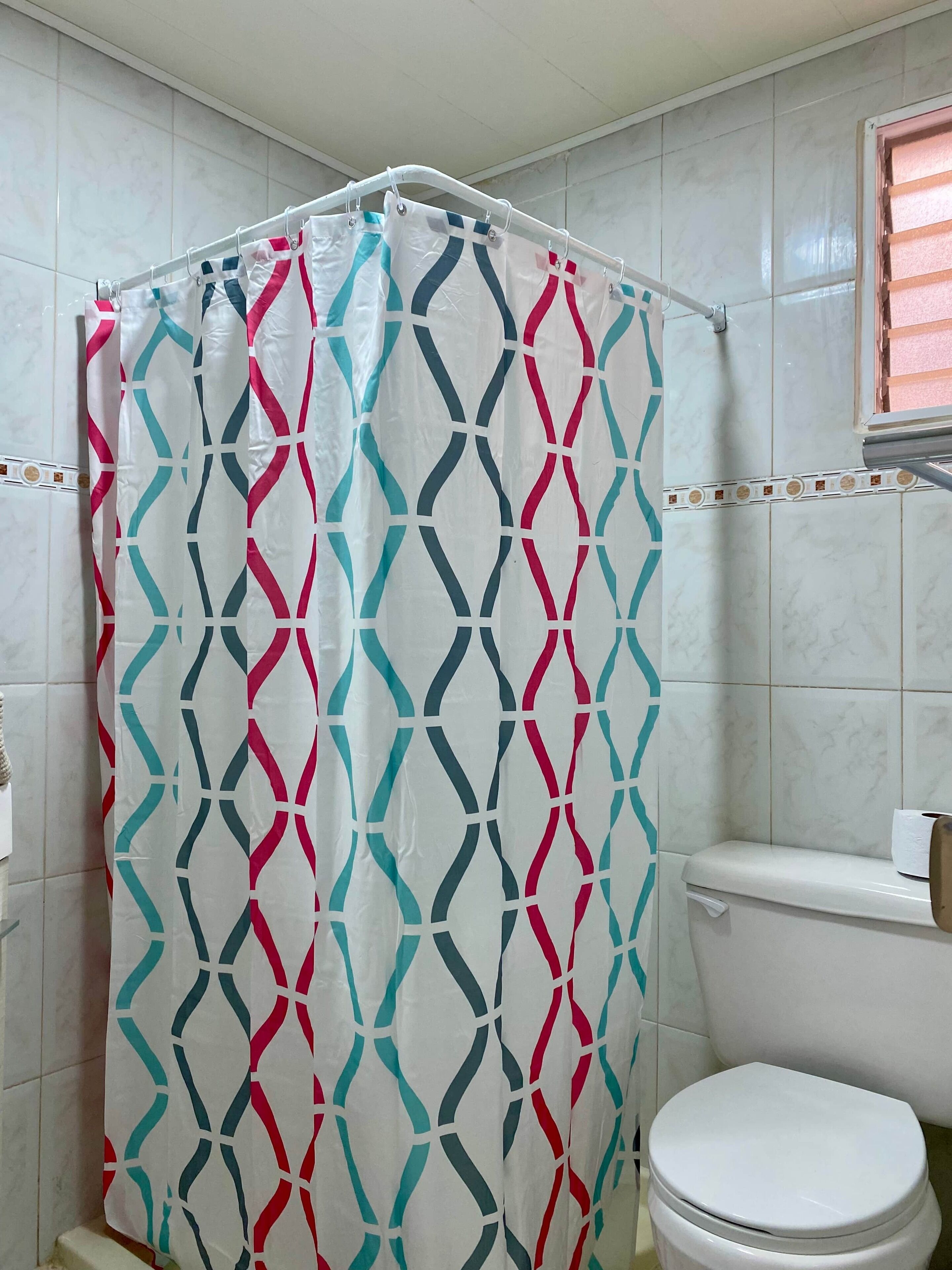 A bathroom with a shower curtain featuring a geometric pattern, a toilet, and a tiled wall.