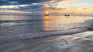 Een strand met rustig water en boten in de verte.